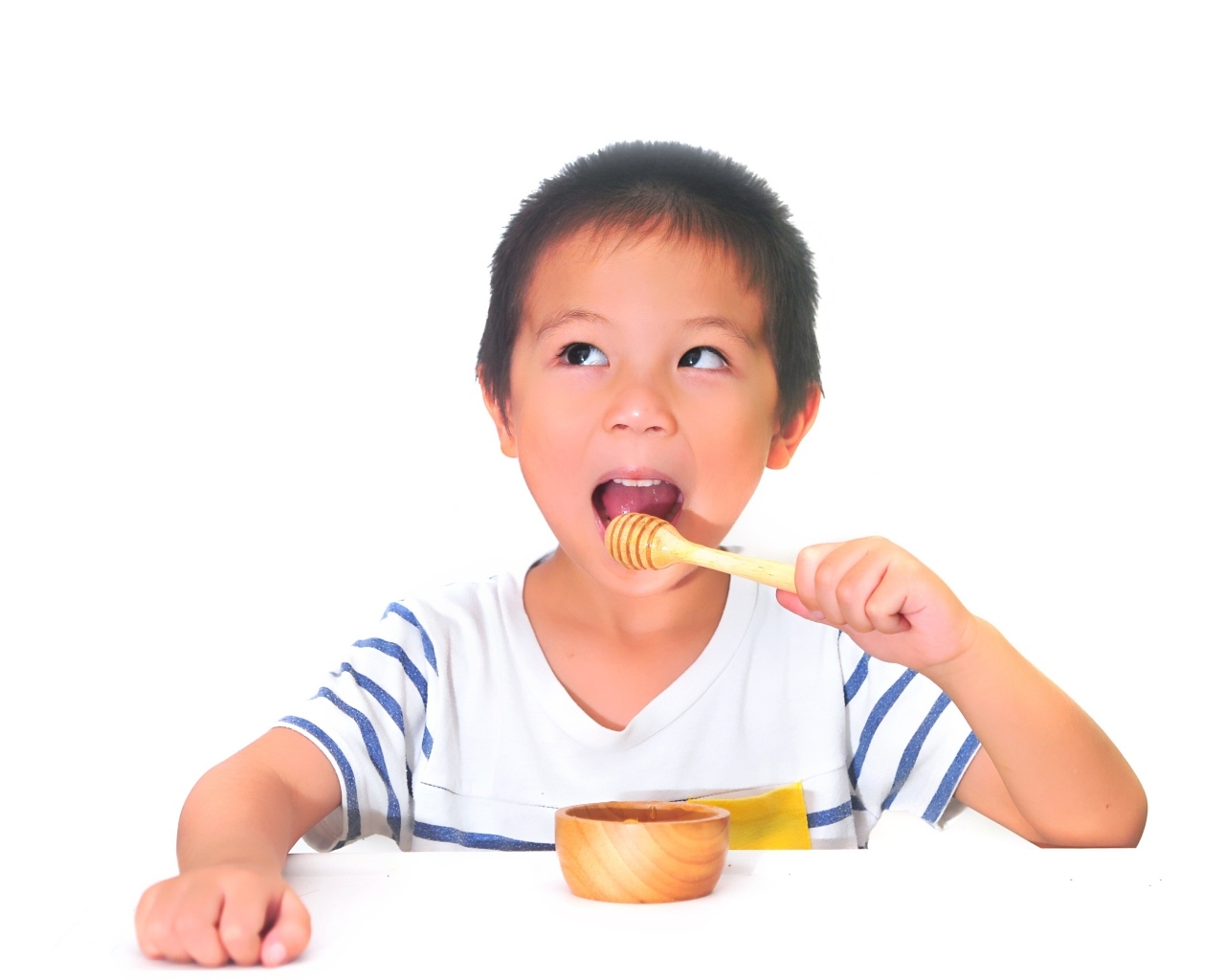 Мальчик азиат ест мед на сером фоне