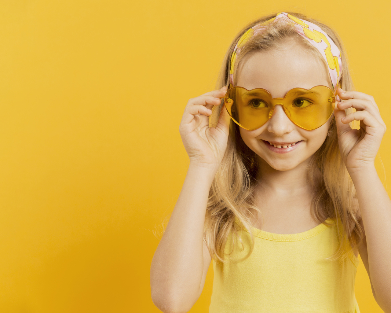 Красивая девочка блондинка в очках в форме сердца на желтом фоне