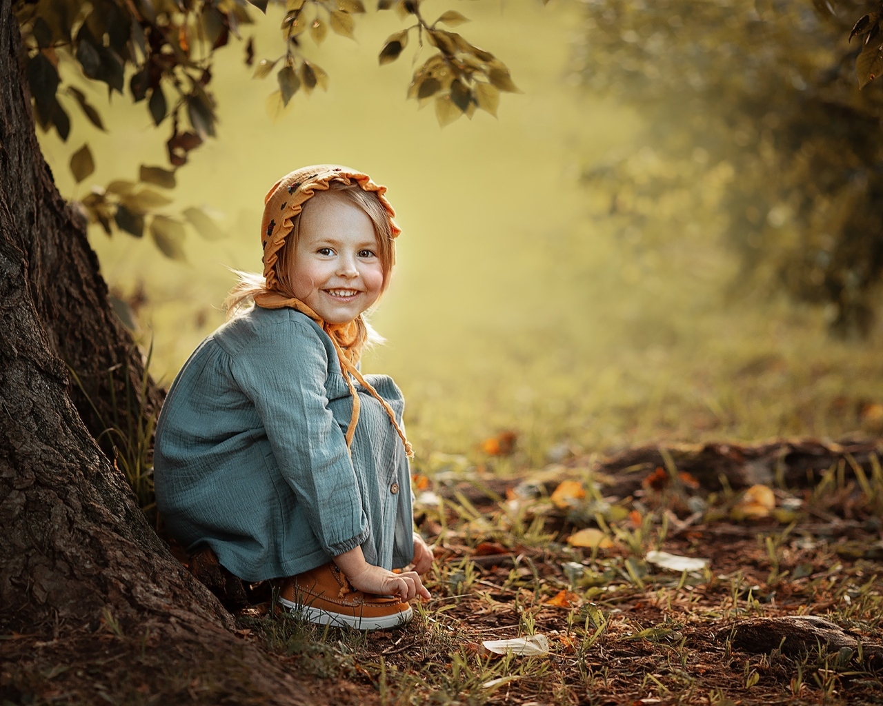 Красивая улыбающаяся девочка сидит под деревом