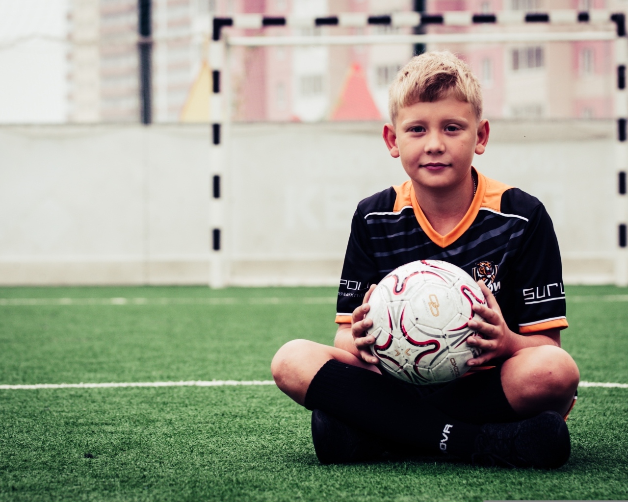 Мальчик футболист сидит на траве с мячом