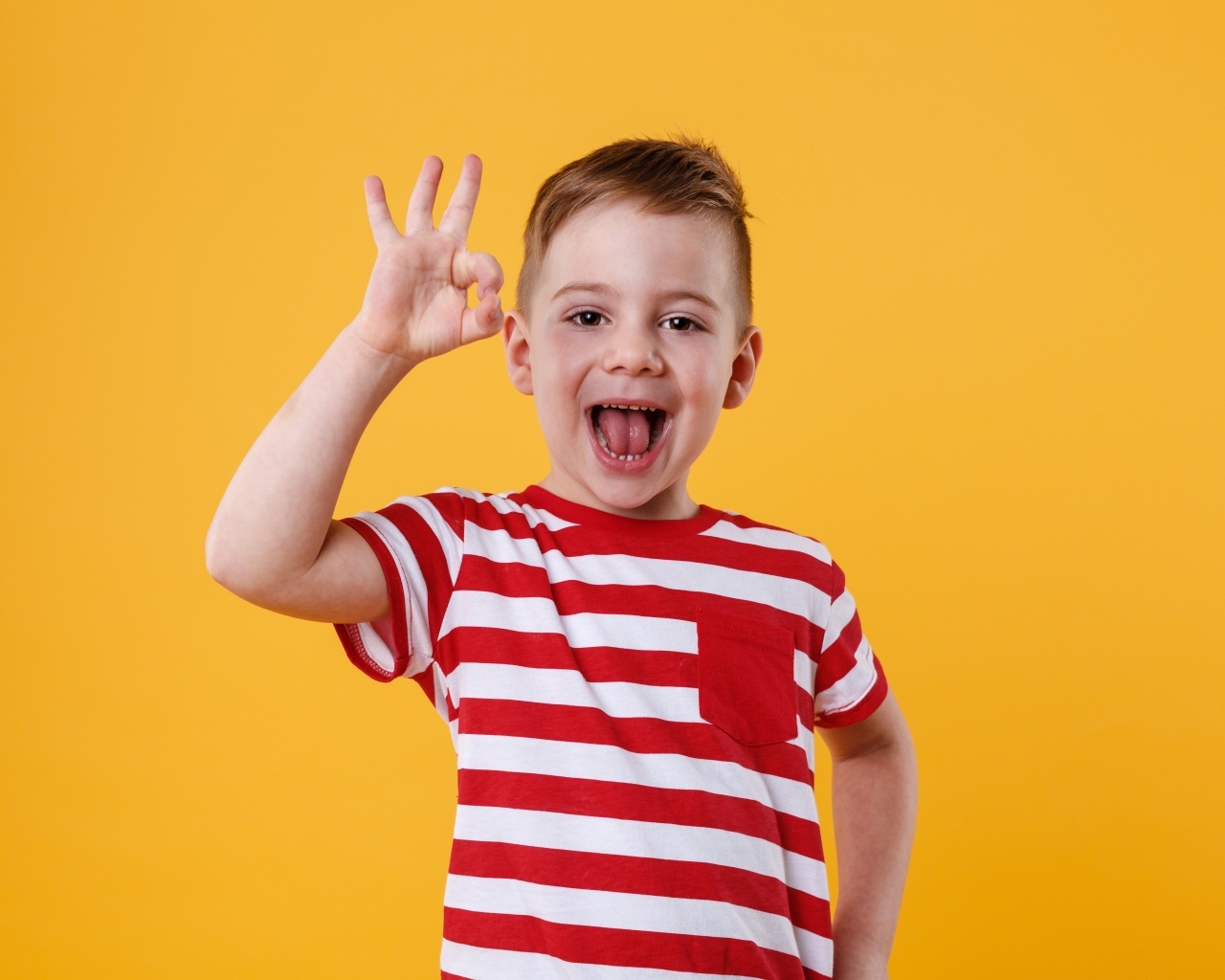 Веселый мальчик в полосатой футболке на оранжевом фоне