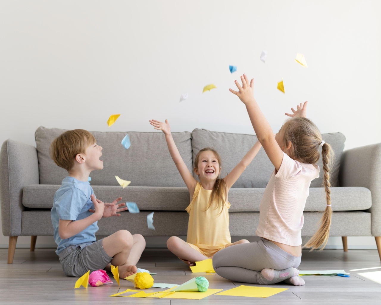 Дети играют на полу  в комнате с серым диваном