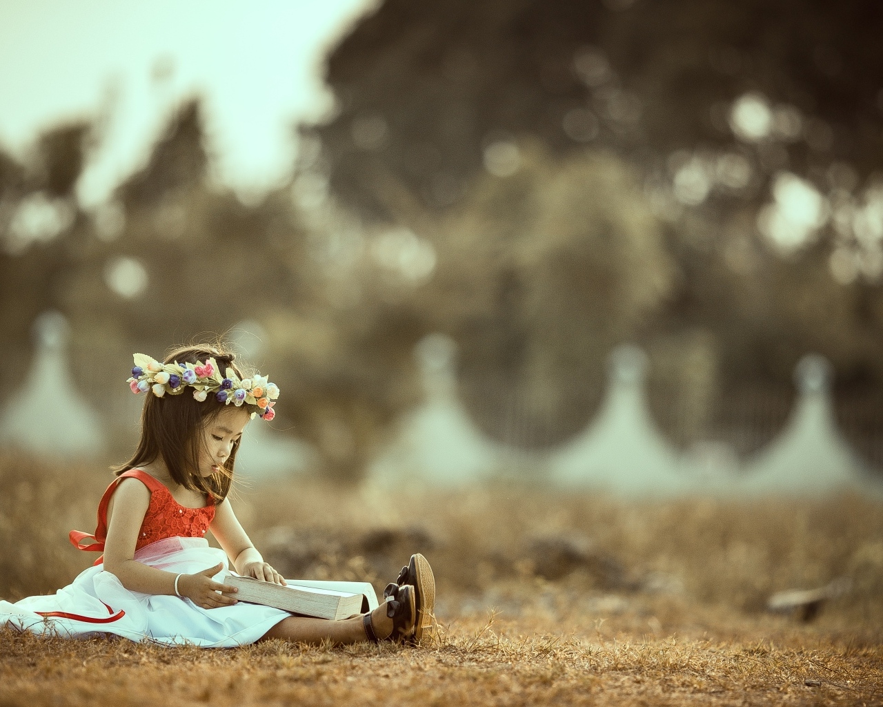 Милая девочка азиатка с венком на голове сидит на земле