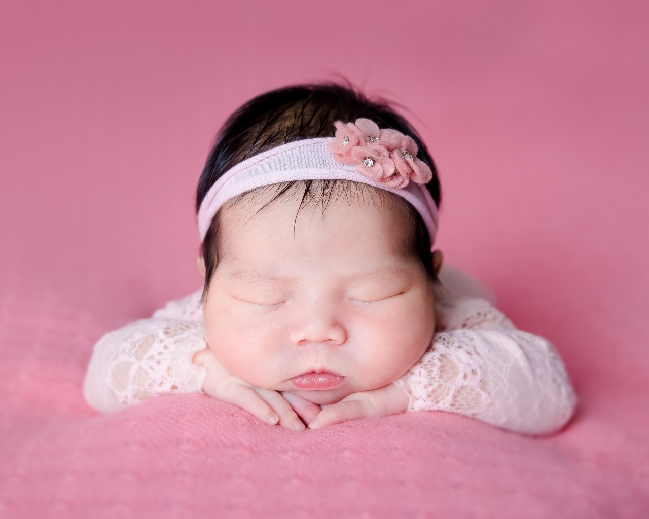 Милая новорожденная девочка с повязкой на голове на розовом фоне
