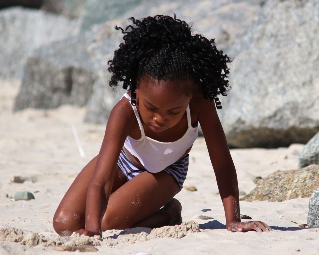 Темнокожая маленькая девочка играет на песке на пляже