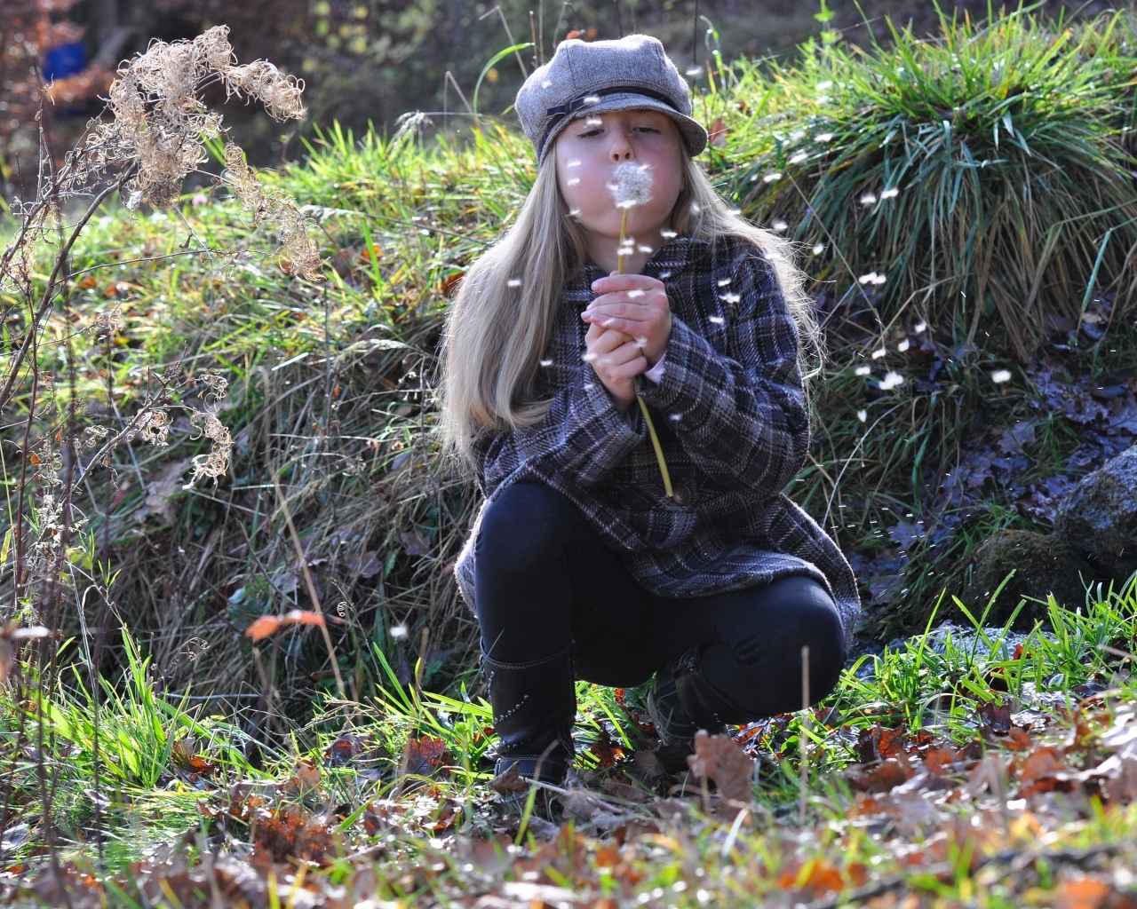 Девочка в кепке дует на одуванчик