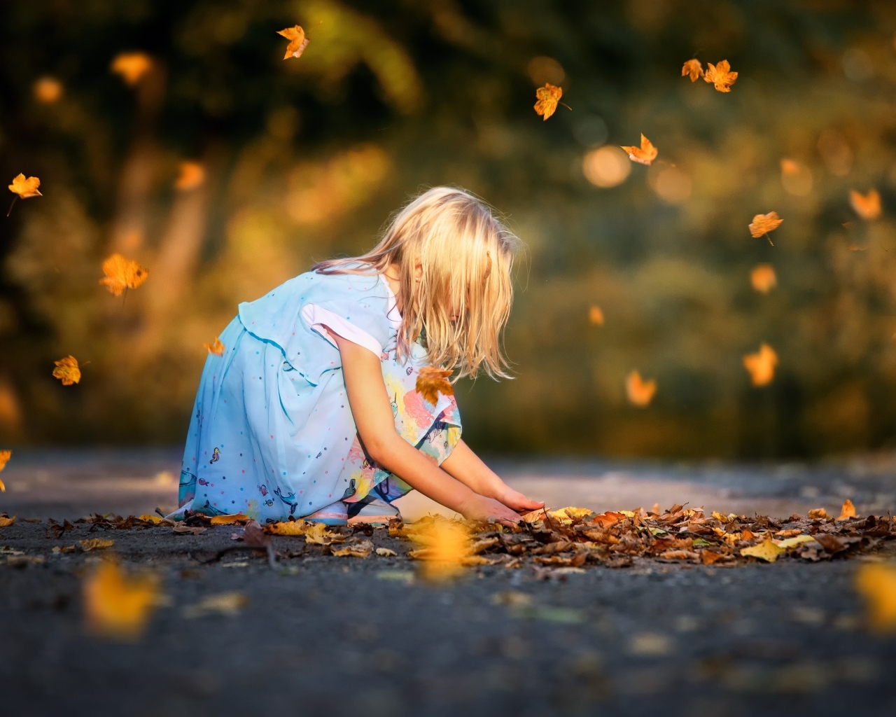 Девочка в платье играет с листьями на дороге