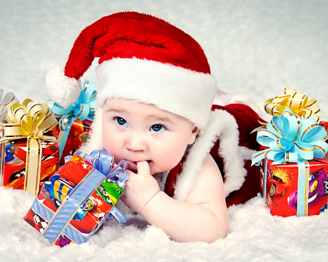 Грудной ребенок в новогодней шапке с подарками на покрывале