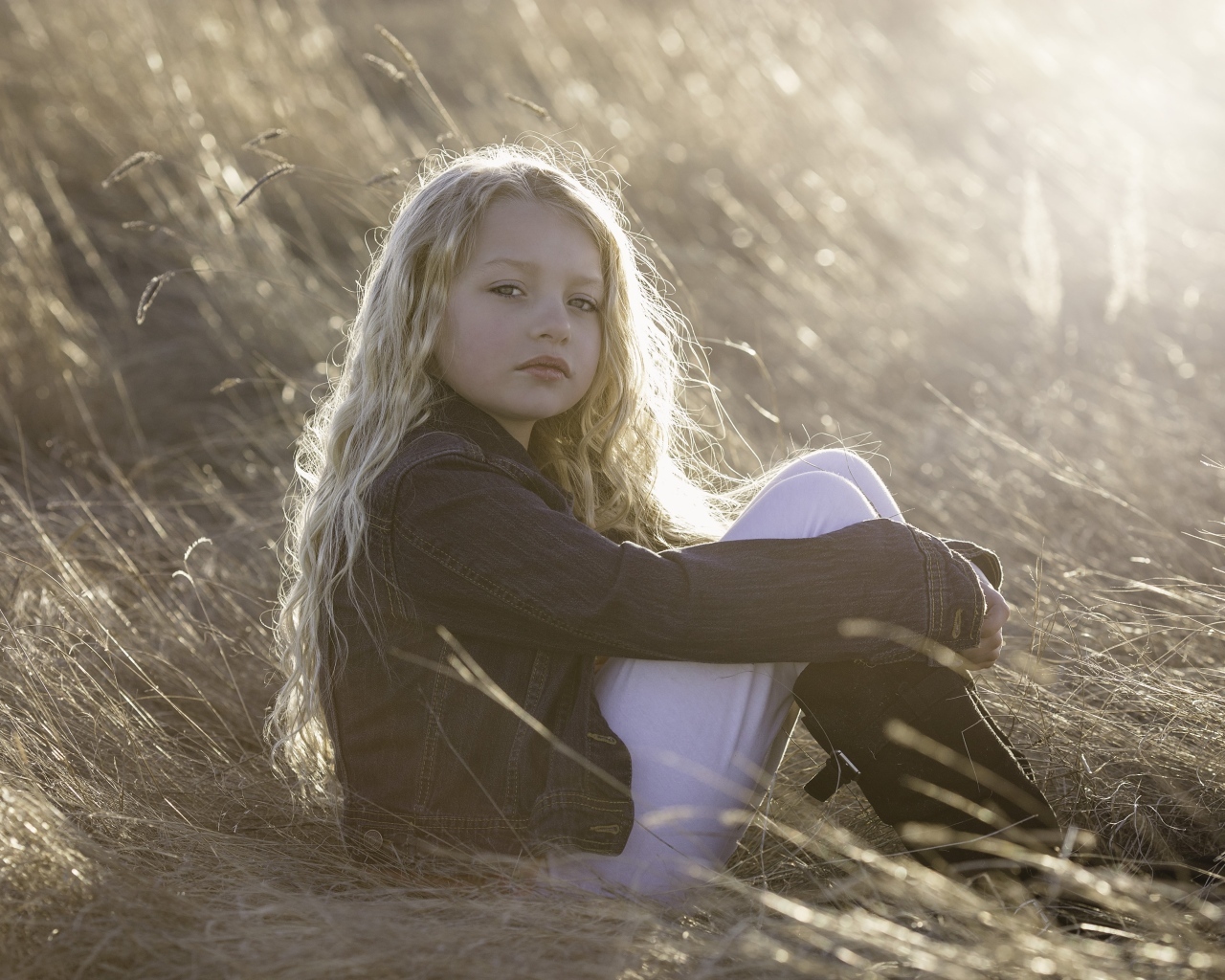 Маленькая светловолосая девочка сидит на сене