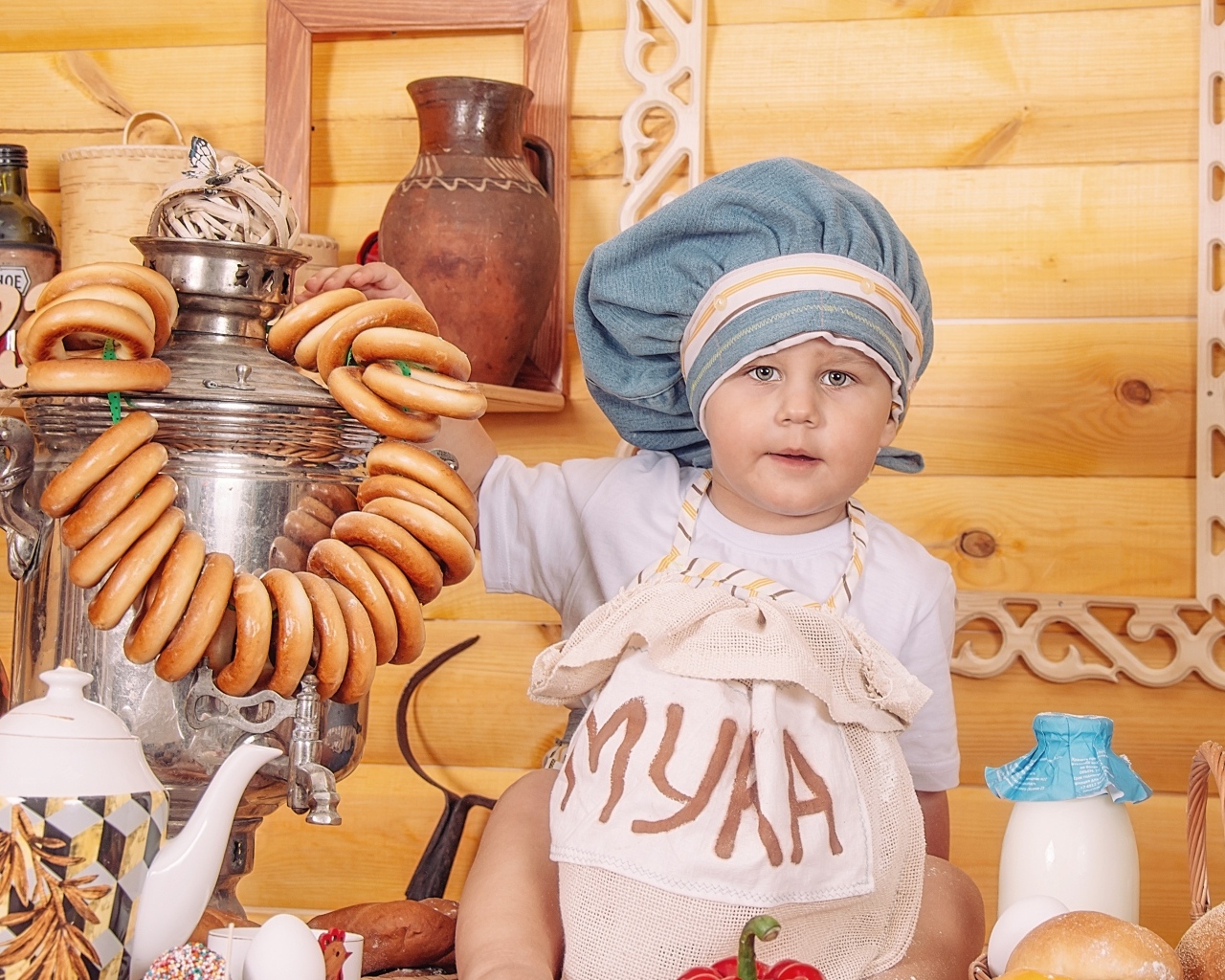 Маленький мальчик повар с продуктами и самоваром на столе