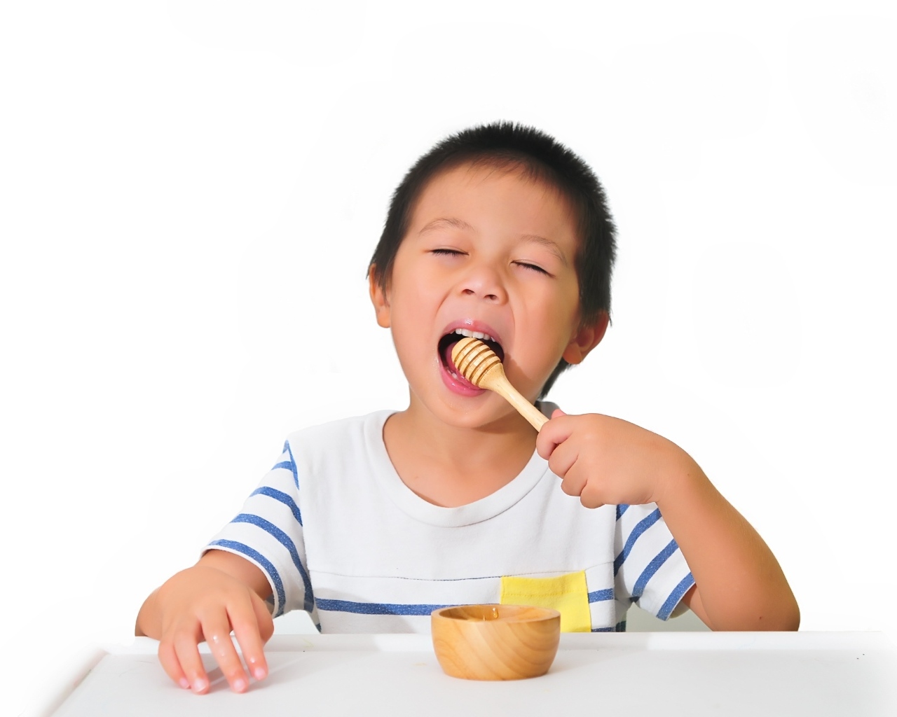Маленький мальчик ест мед на белом фоне