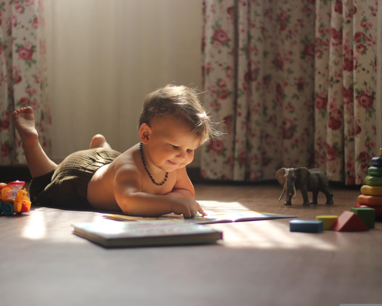 Маленький мальчик читает книгу на полу с игрушками