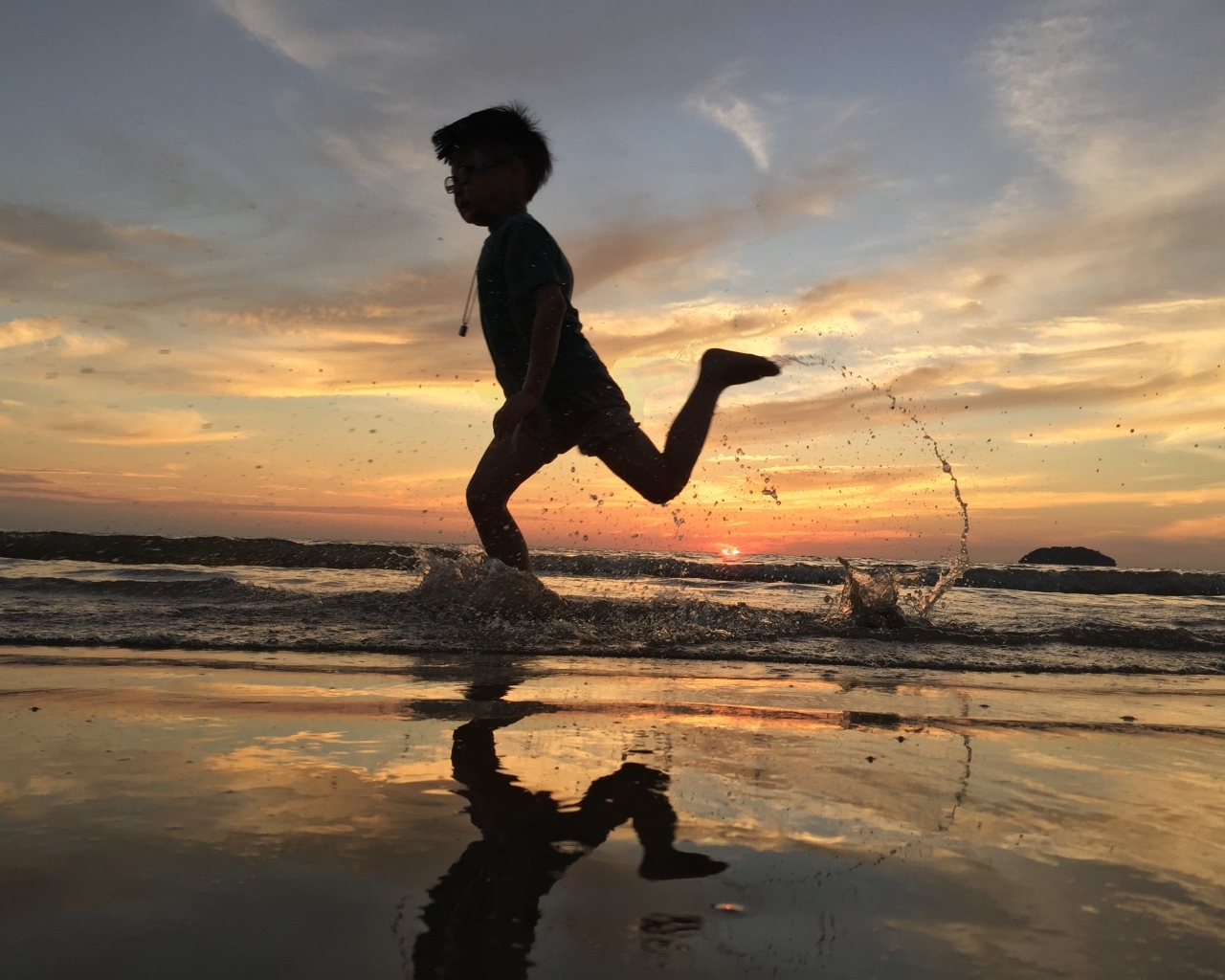 Маленький мальчик бежит по воде на закате
