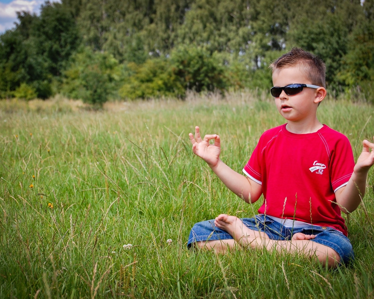 Маленький мальчик в очках медитирует на зеленой траве