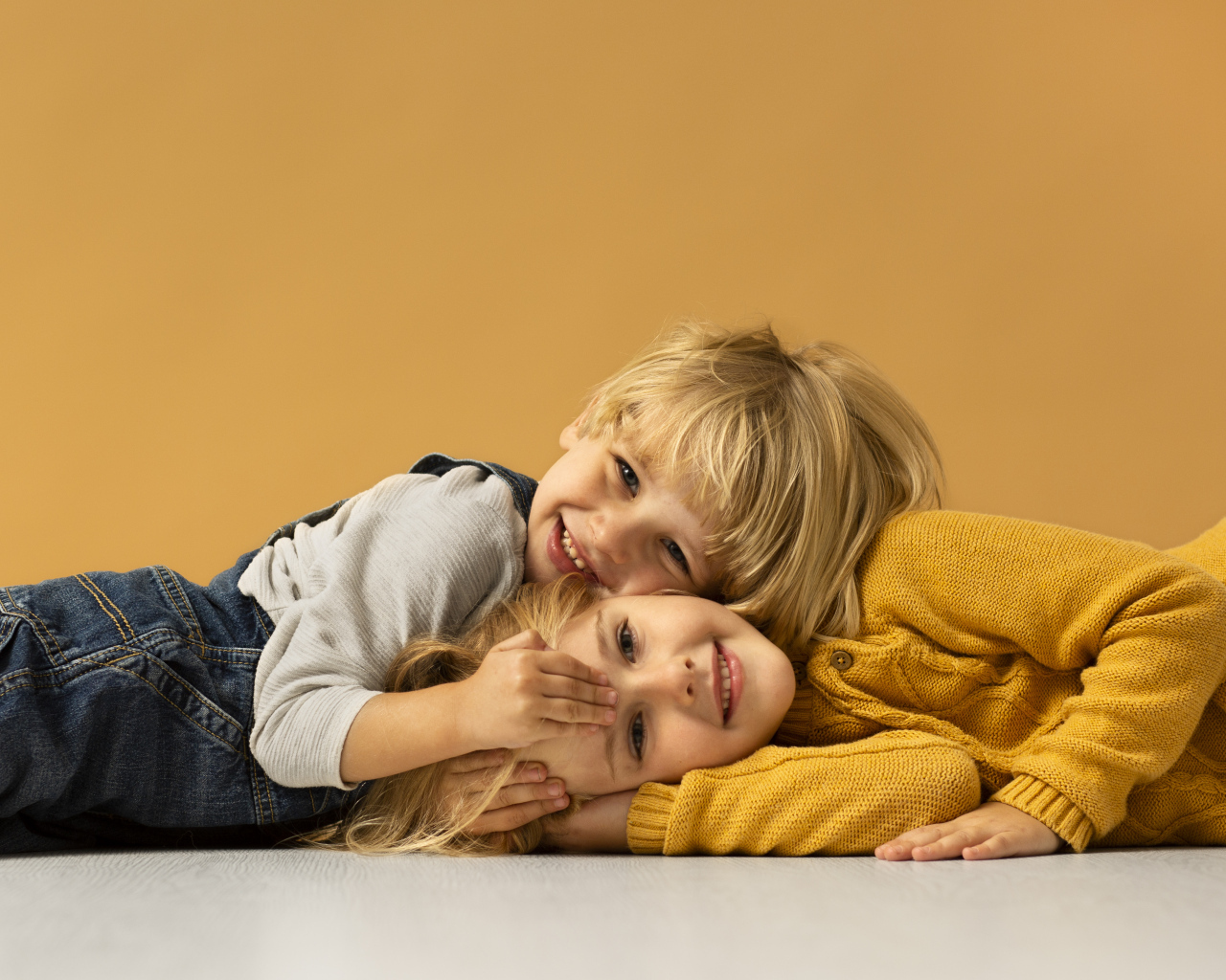Маленькие брат и сестра лежат на полу на желтом фоне