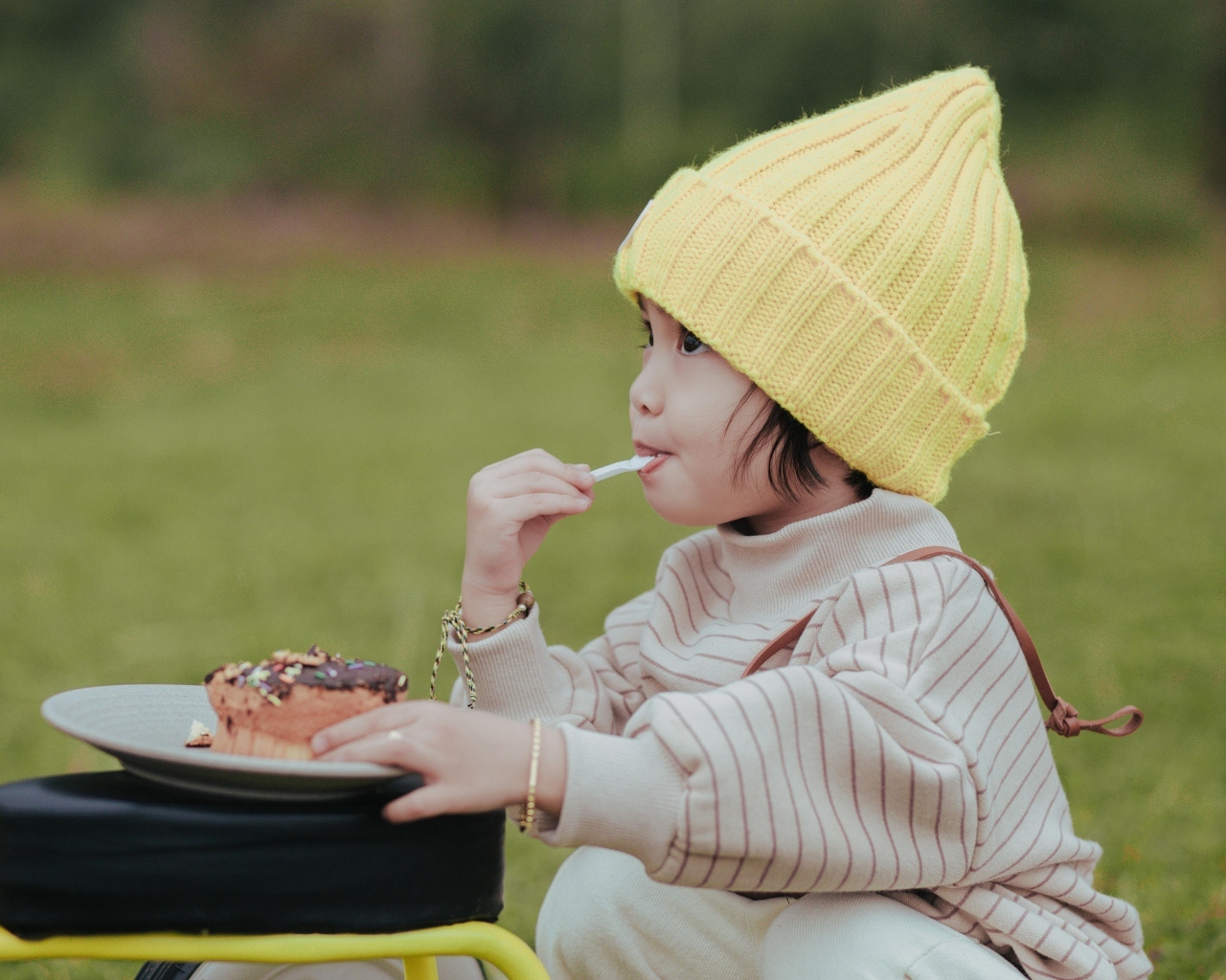 Маленькая девочка в желтой шапке ест пирожное