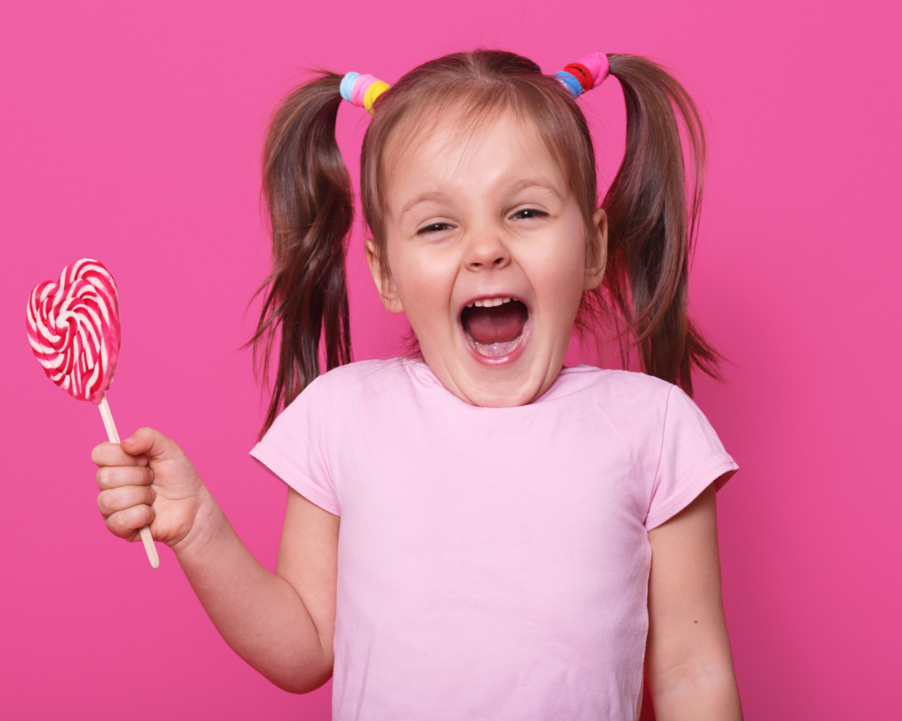 Маленькая девочка с леденцом на розовом фоне