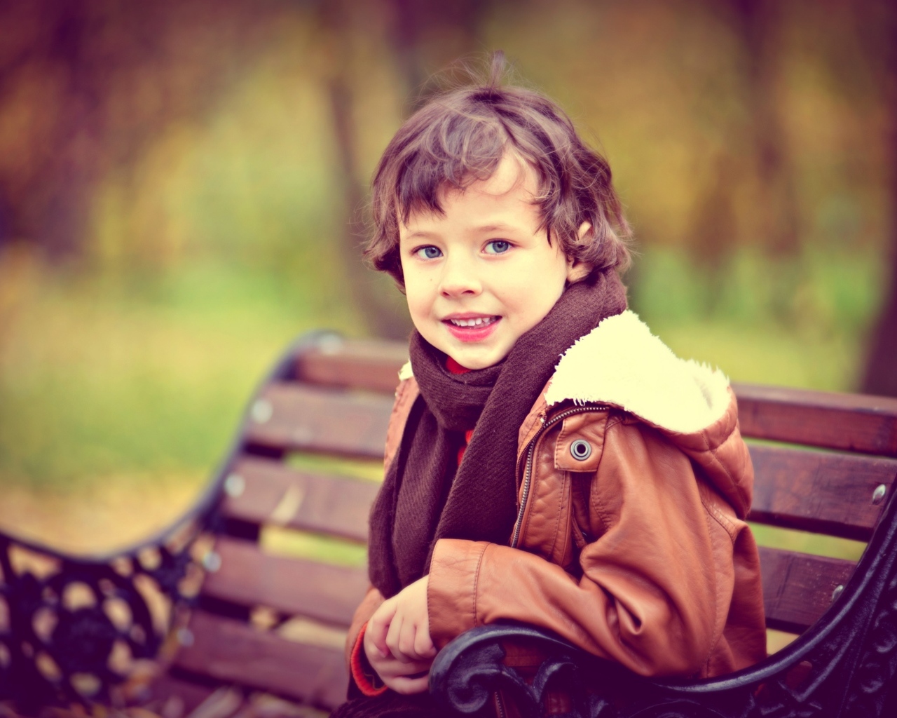 Маленький улыбающийся мальчик на лавке в парке