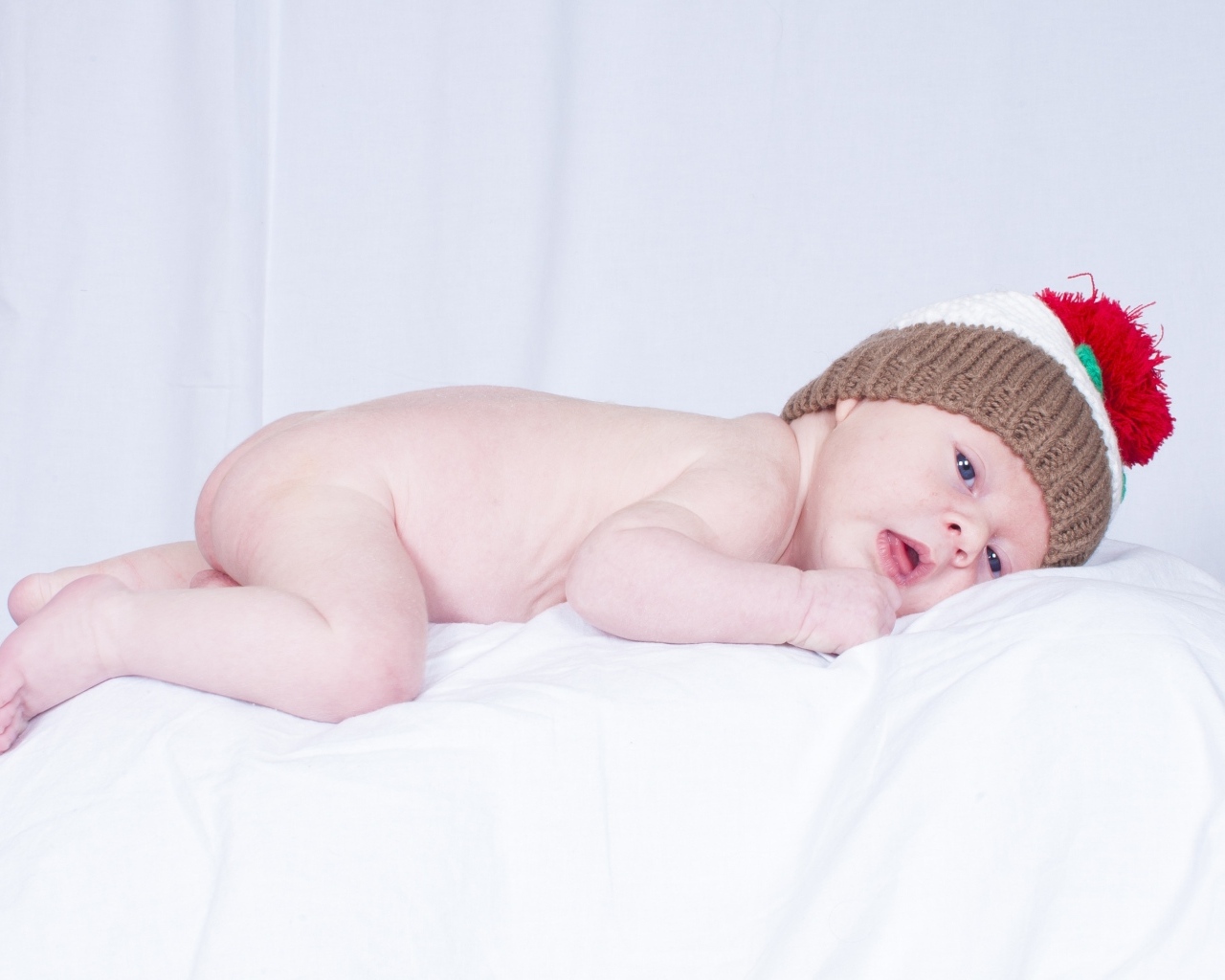 Новорожденный малыш в шапке на белой подушке
