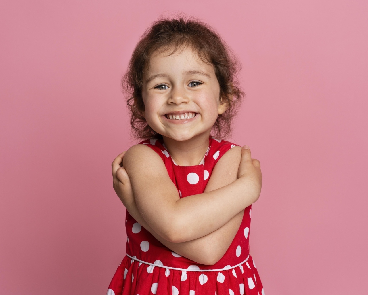 Улыбающаяся маленькая девочка в красном платье на розовом фоне