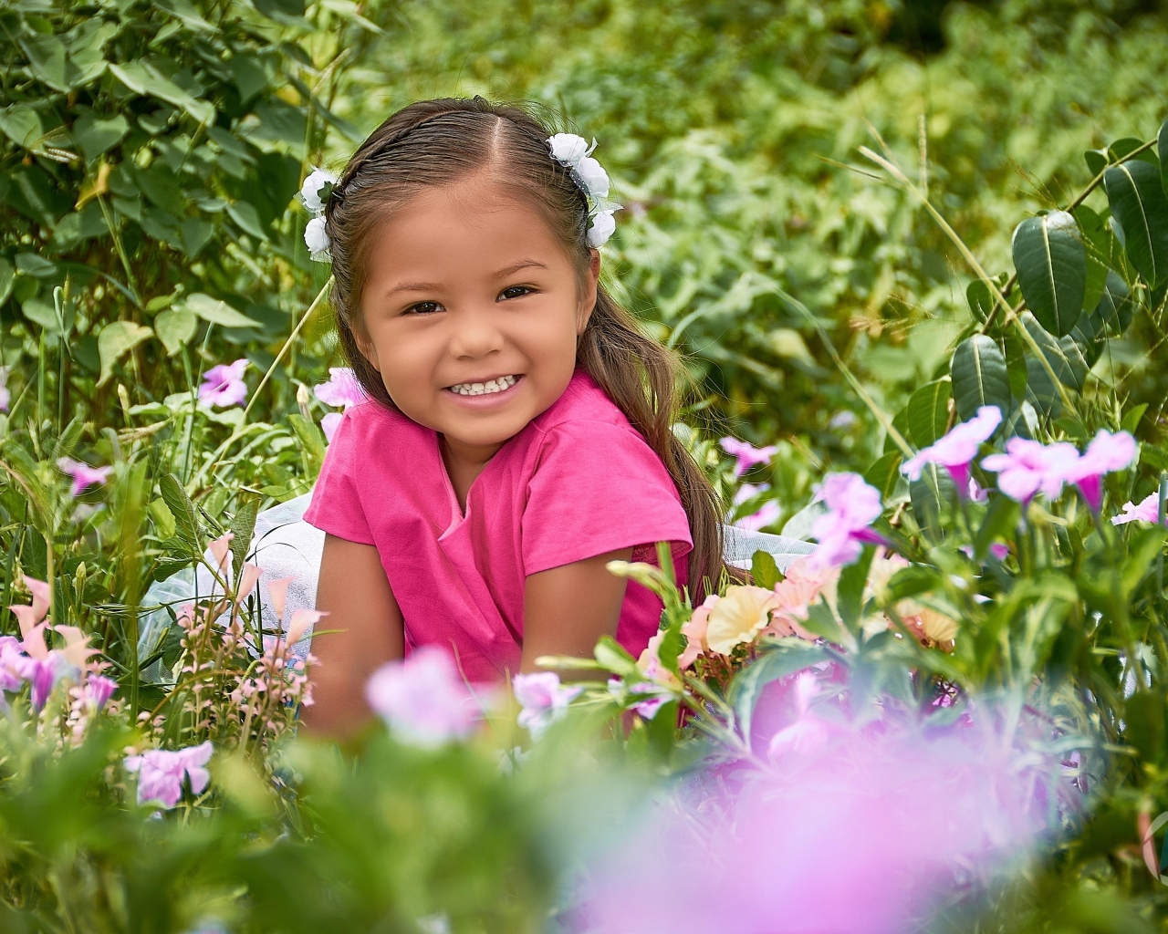 Улыбающаяся маленькая девочка сидит в цветах