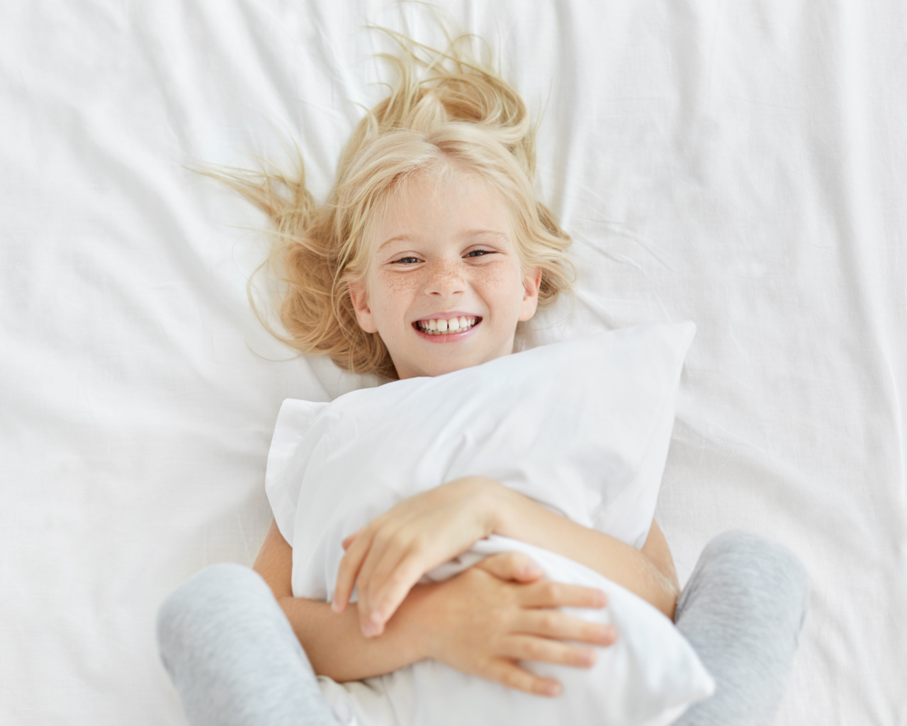Улыбающаяся маленькая девочка с подушкой на кровати