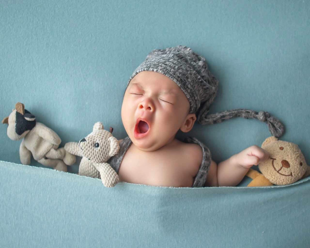 Зевающий малыш с игрушками под серым покрывалом