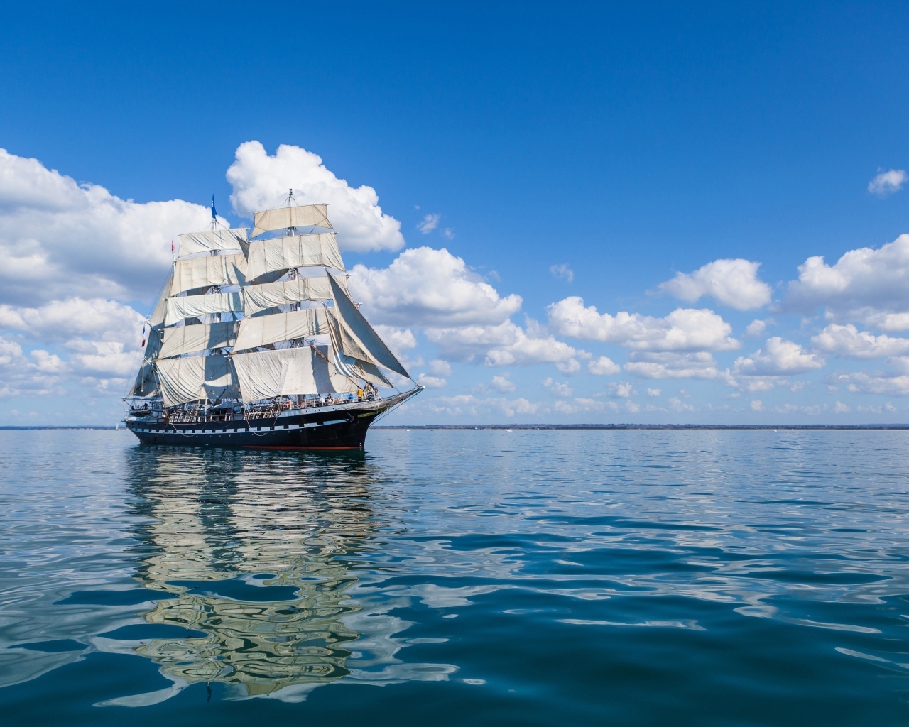 Большой корабль с белыми парусами на фоне голубого неба с облаками в море