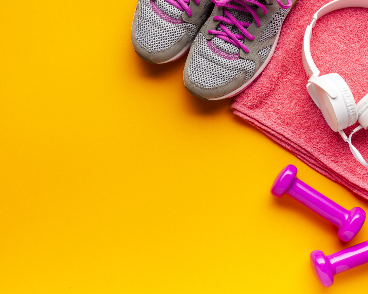 Розовые гантели, наушники, кроссовки и полотенце на желтом фоне