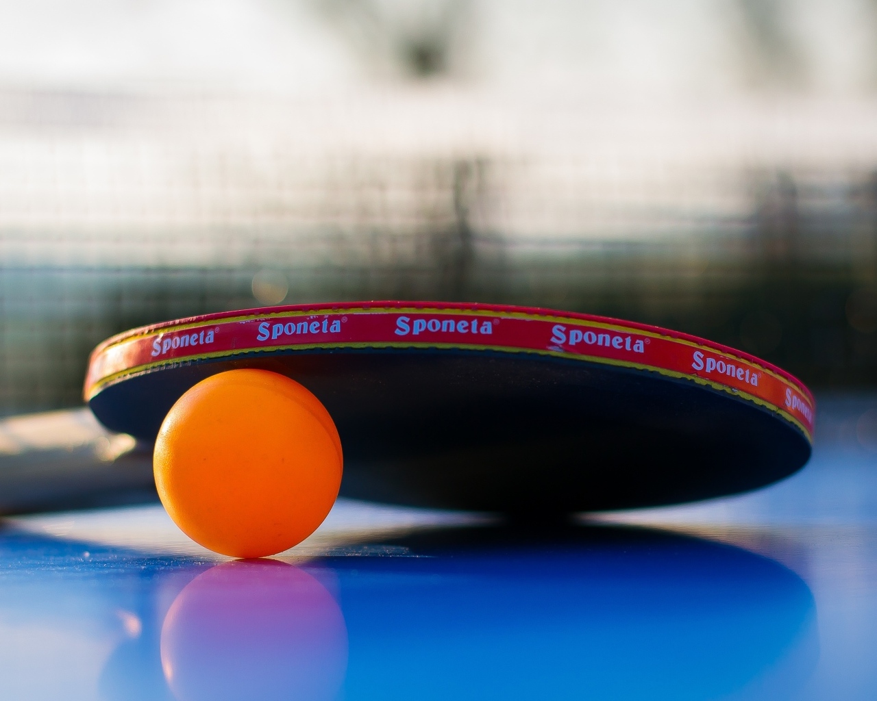 Ракетка и оранжевый мяч для пинг понга на столе