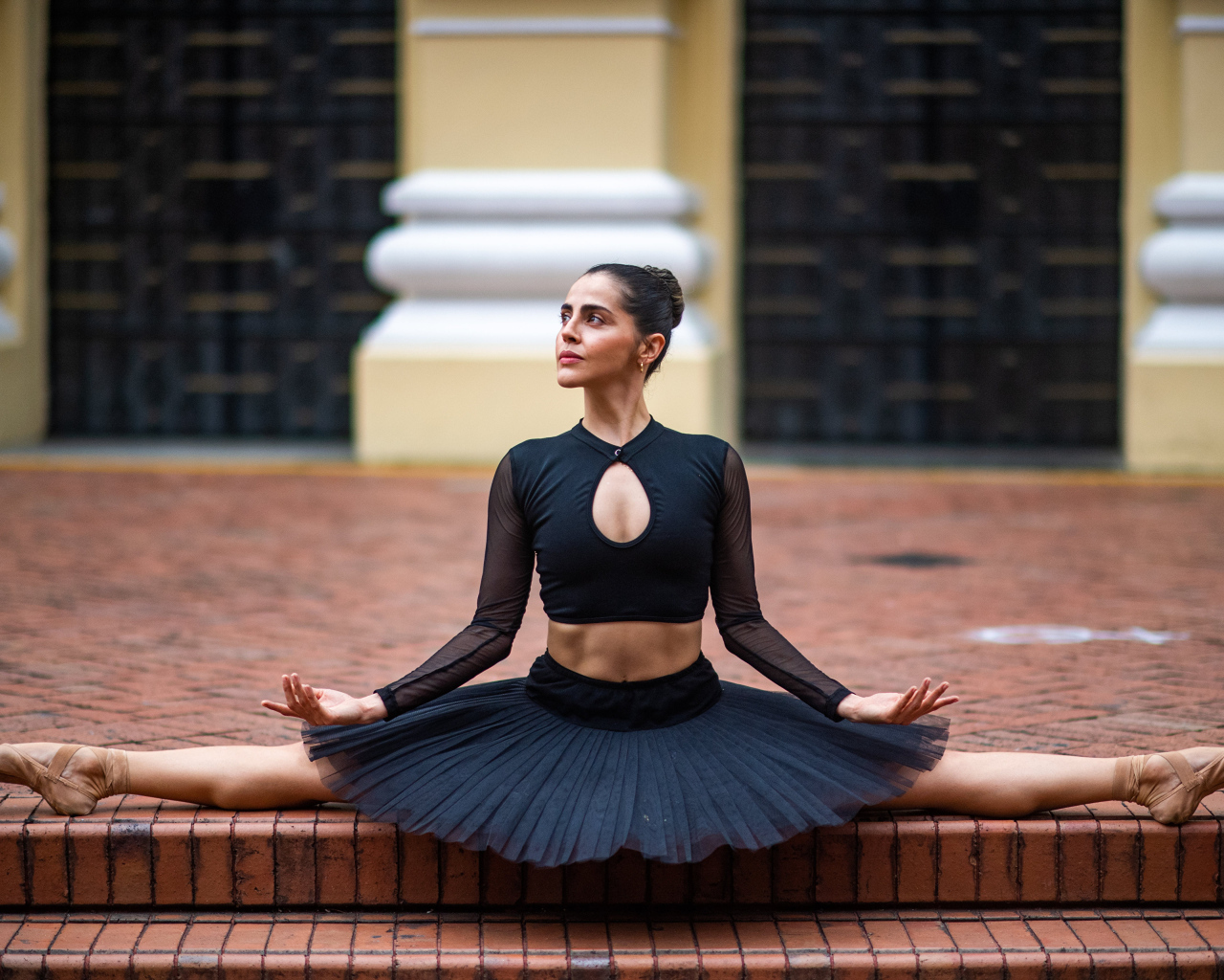 Девушка балерина в черном наряде сидит на шпагате