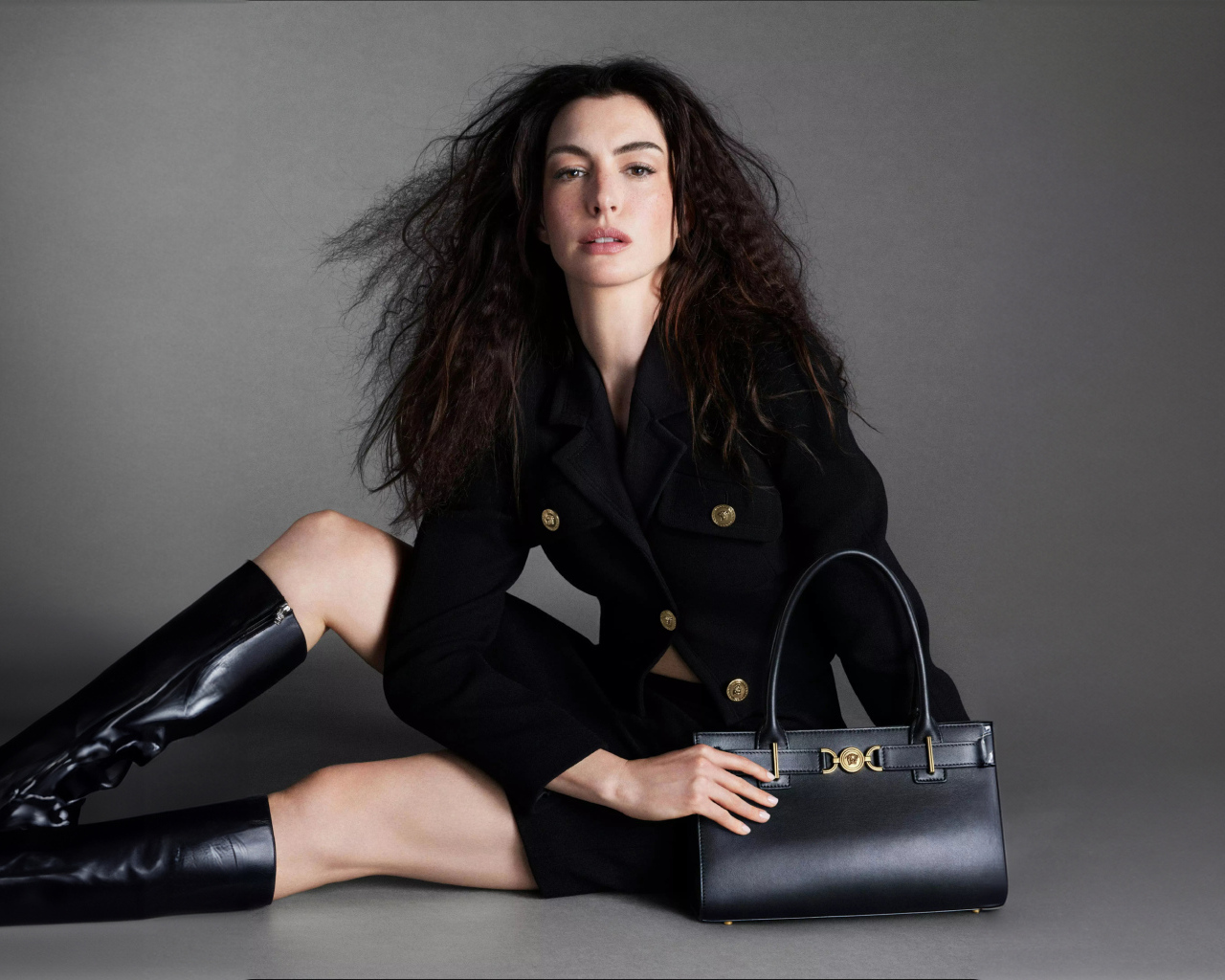 Актриса Энн Хэтэуэй в черных сапогах с сумочкой на сером фоне