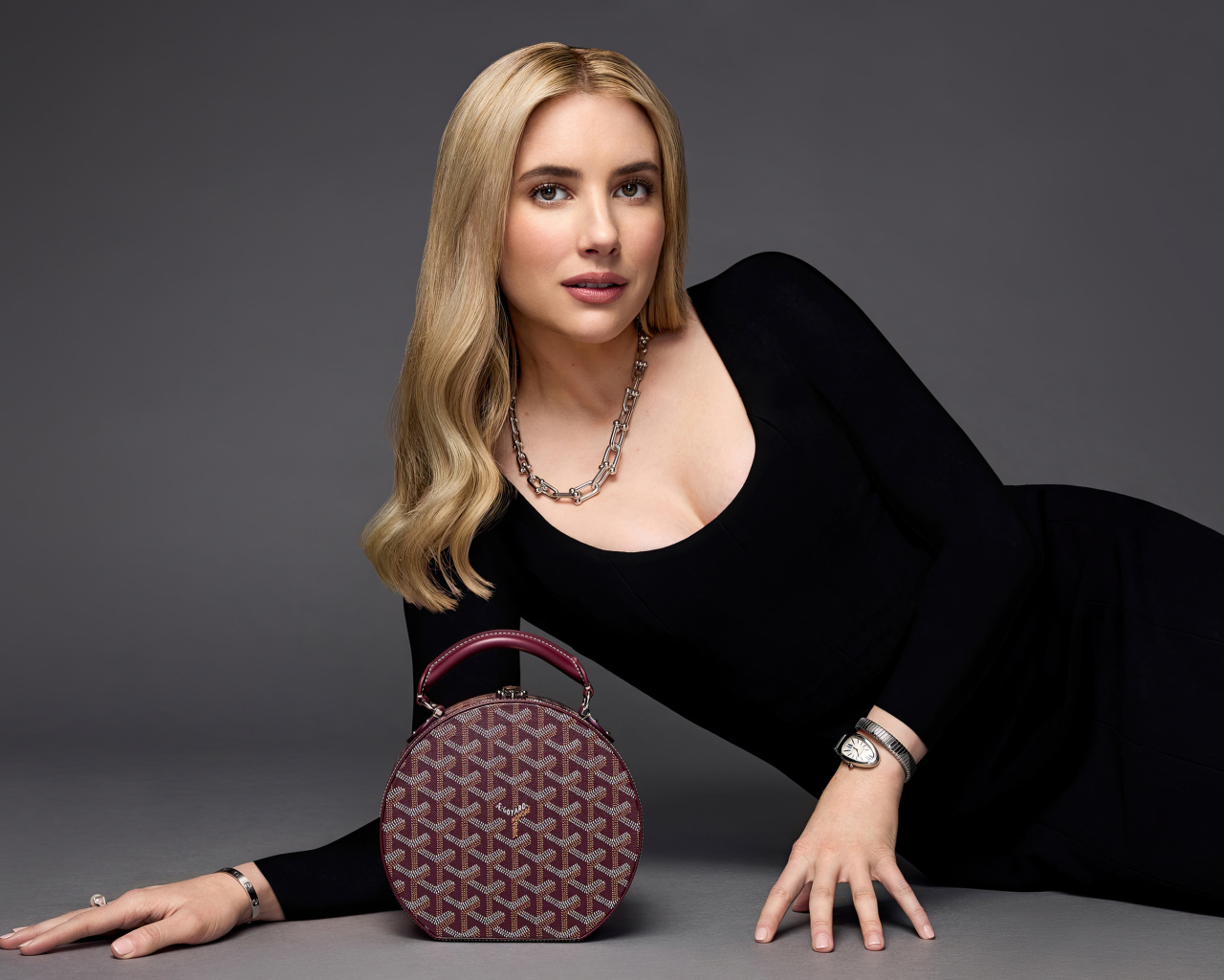 Актриса Эмма Робертс в черном платье с сумочкой лежит на сером фоне