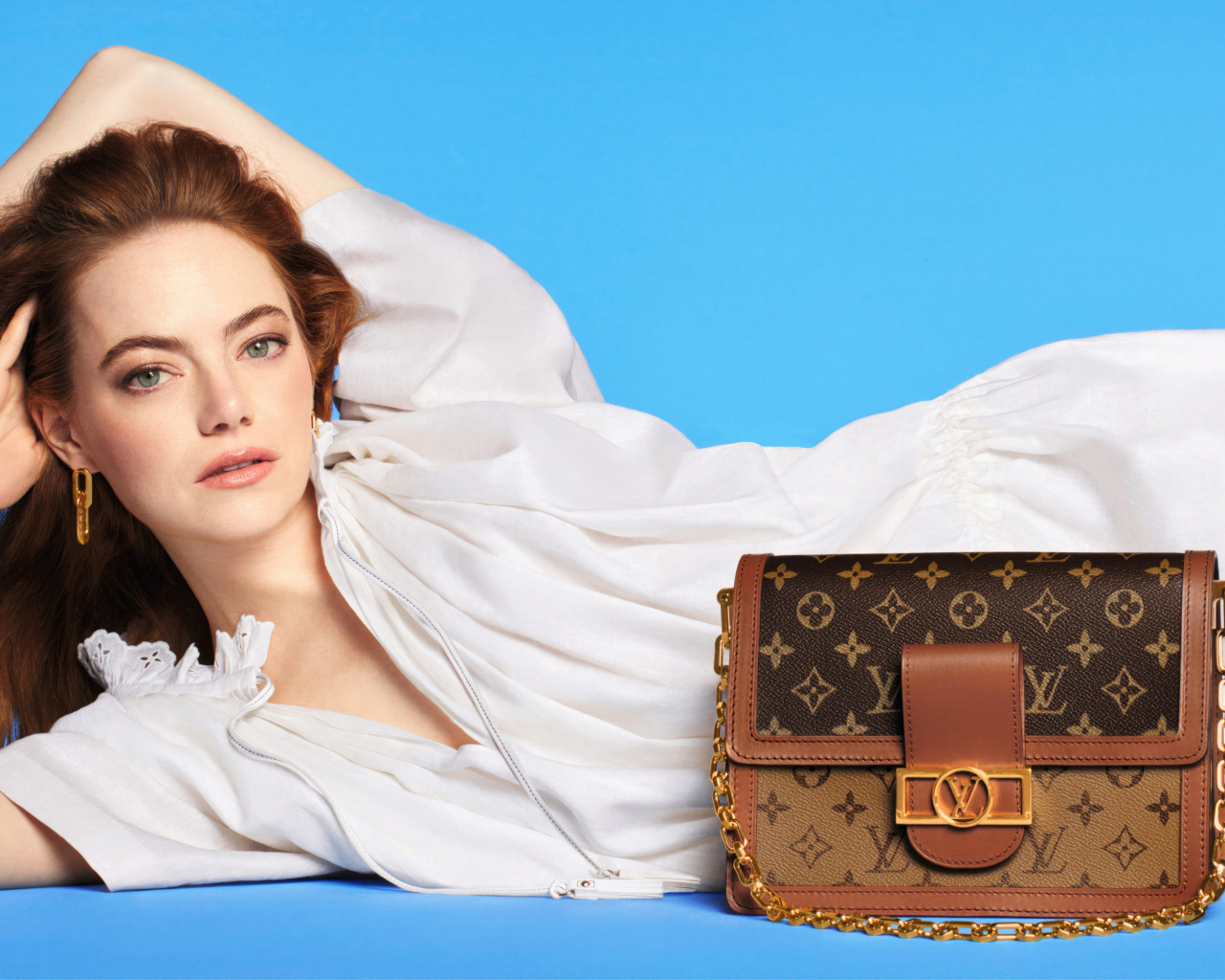 Актриса Эмма Стоун с сумочкой Louis Vuitton на голубом фоне