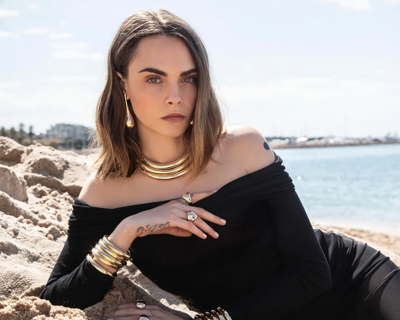 Кара Делевинь в черном платье лежит на песке