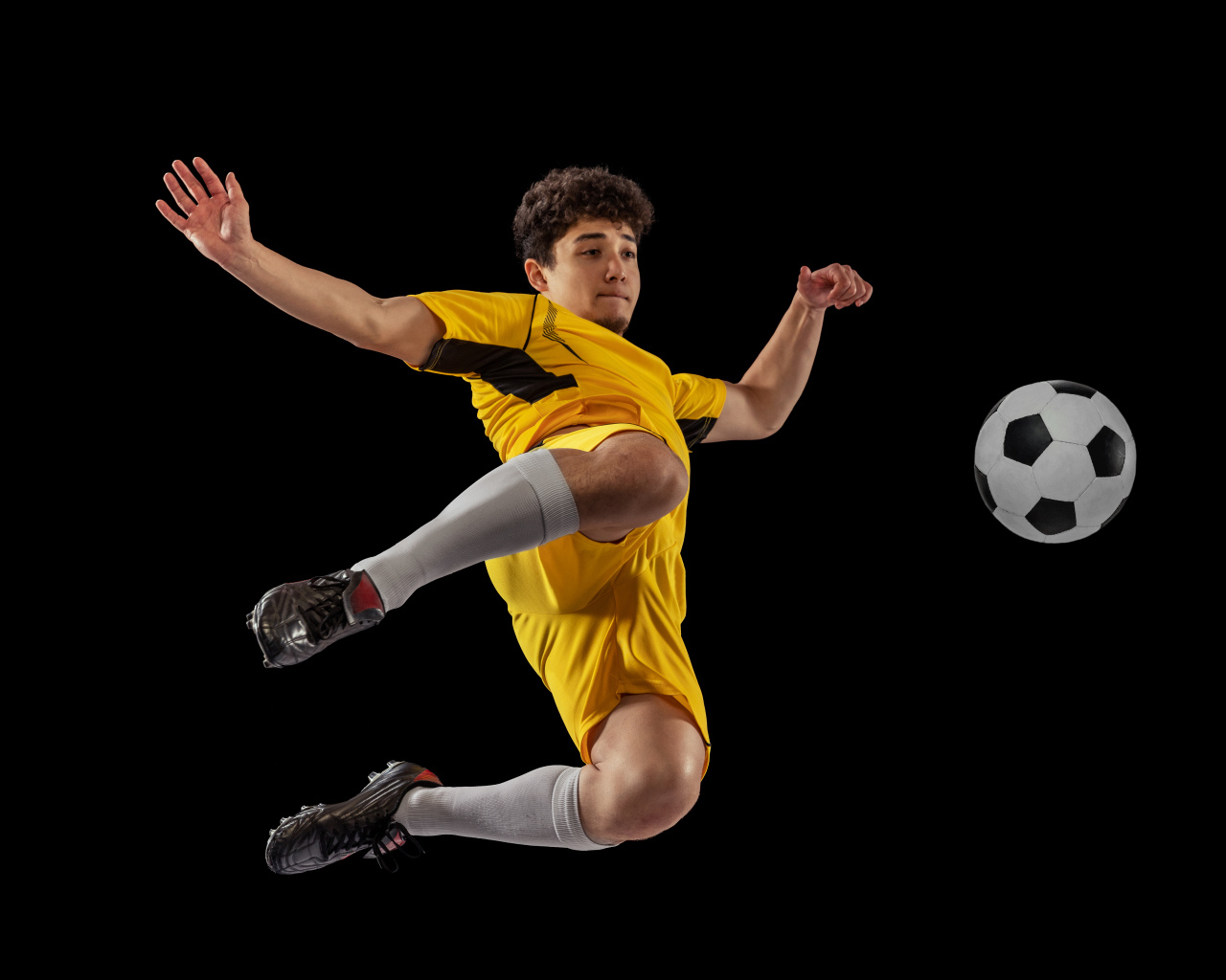 Мужчина футболист отбивает мяч на черном фоне