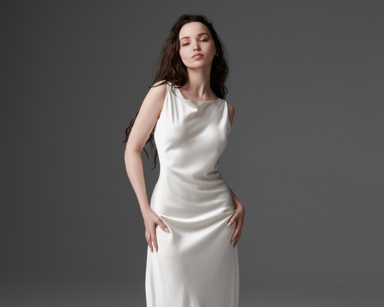 Стройная девушка актриса Дав Кэмерон в белом платье на сером фоне