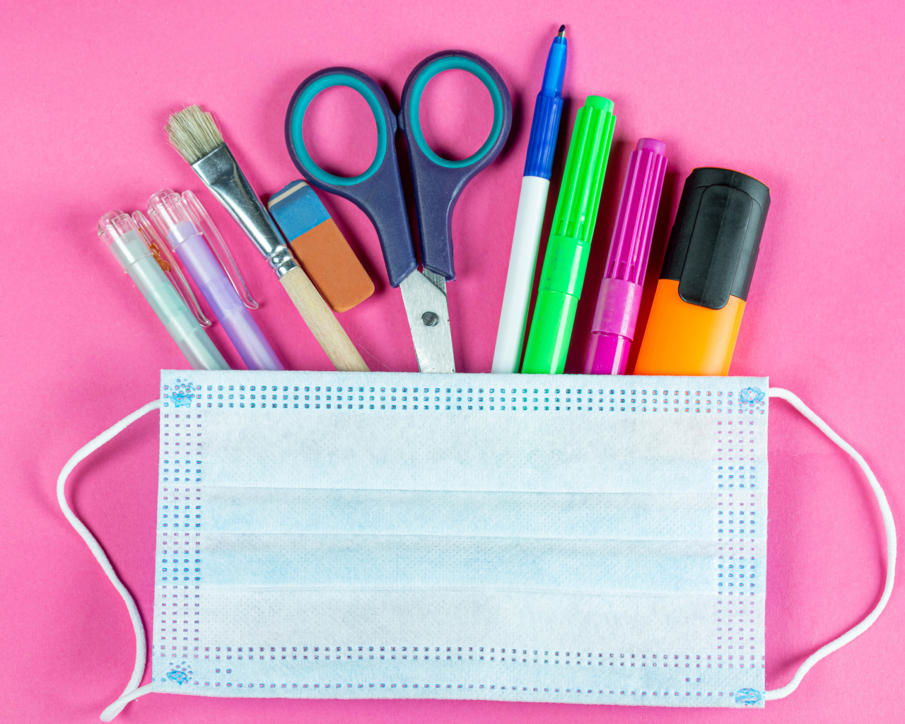 Канцелярские предметы и медицинская маска на розовом фоне