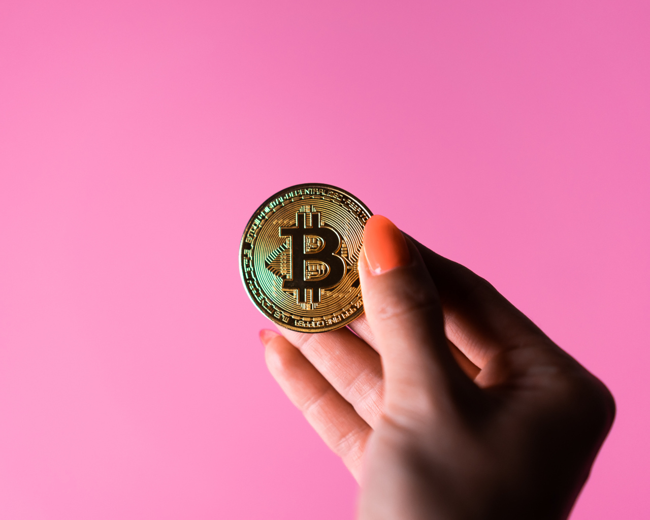 Золотая монета биткоин в руке девушки на розовом  фоне