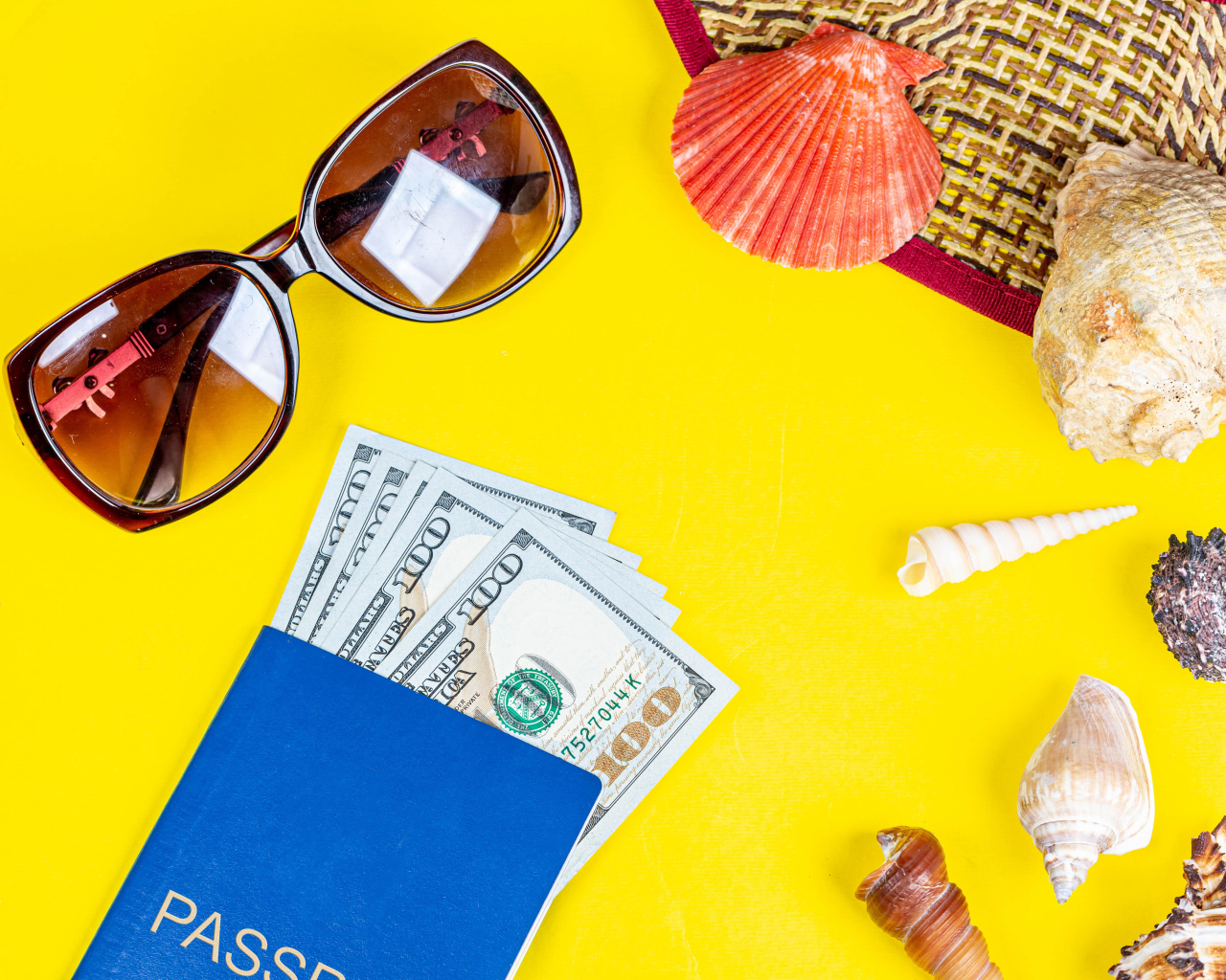Очки, доллары с паспортом и ракушки на желтом фоне
