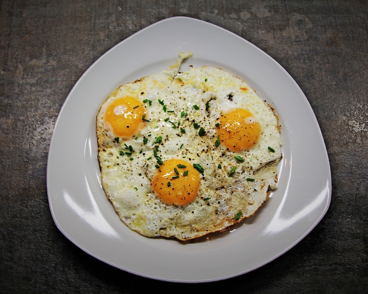 Яичница глазунья в тарелке на сером столе