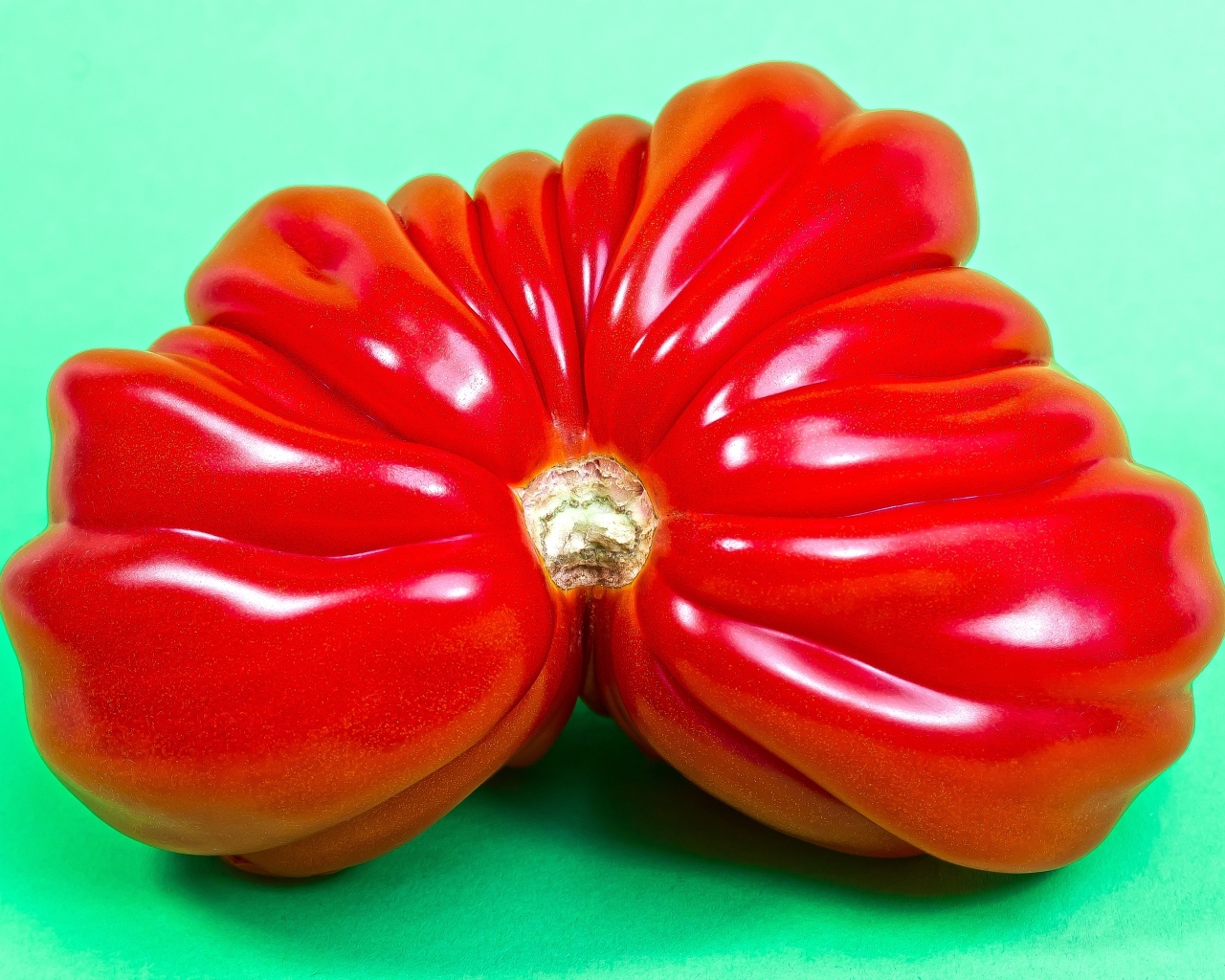 Большой спелый красный томат на зеленом фоне