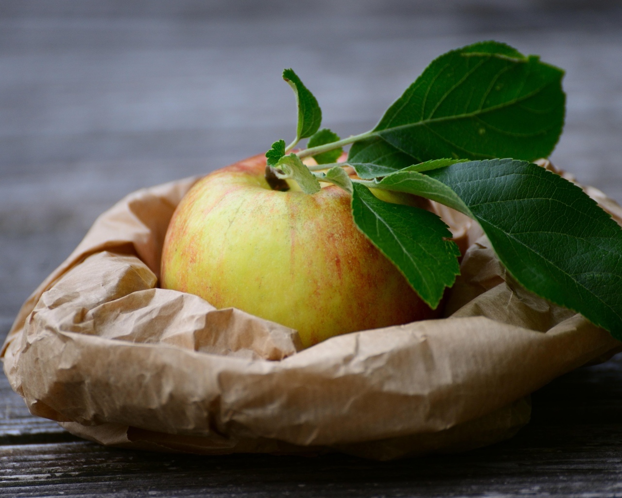 Яблоко с зелеными листьями на бумаге
