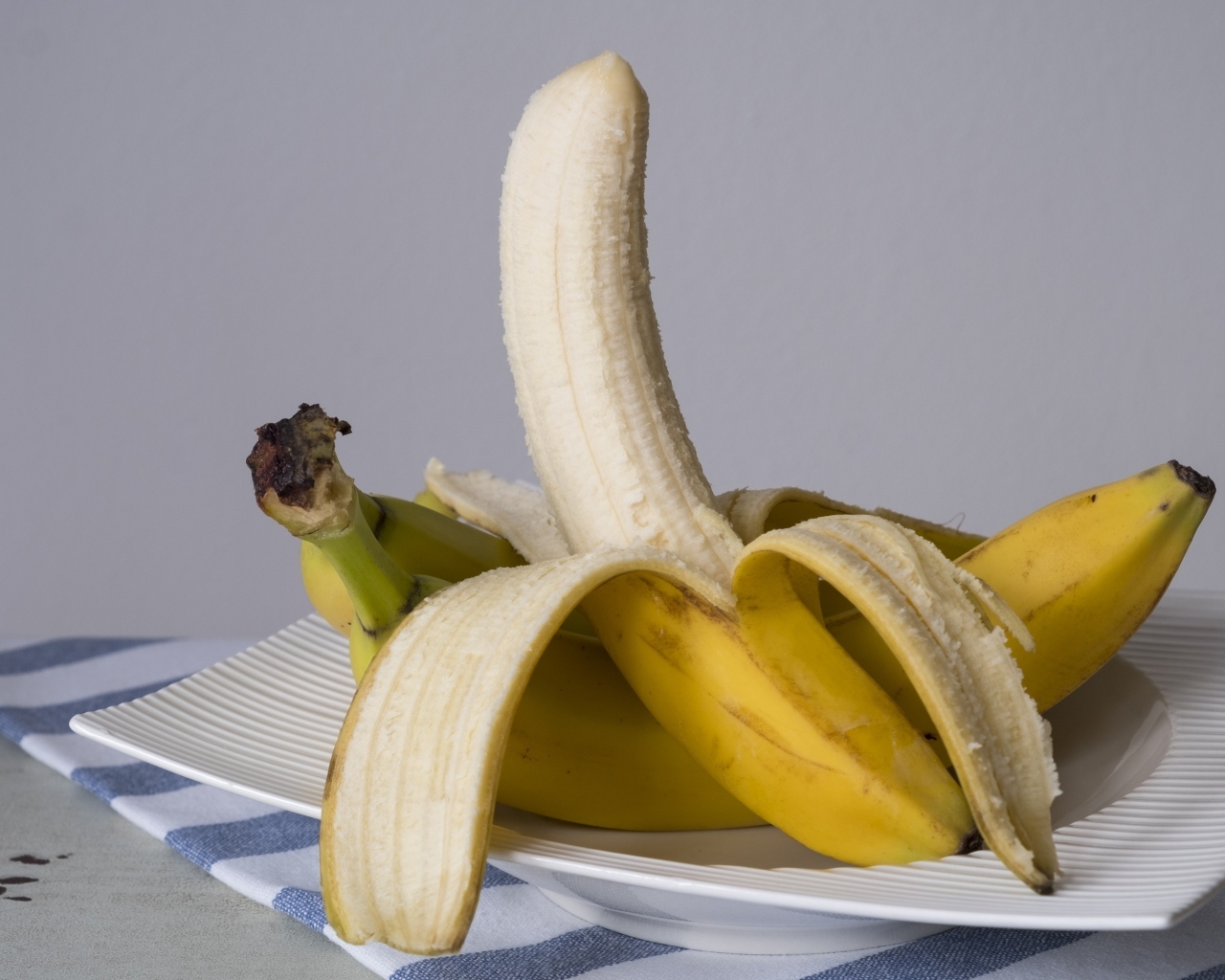 Очищенный банан на тарелке на сером фоне