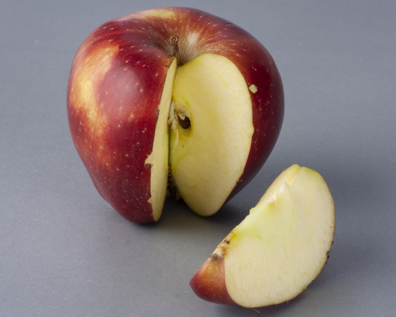 Разрезанное красное яблоко на сером фоне