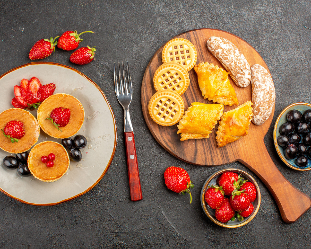 Печенье и оладьи на столе с ягодами клубники и виноградом