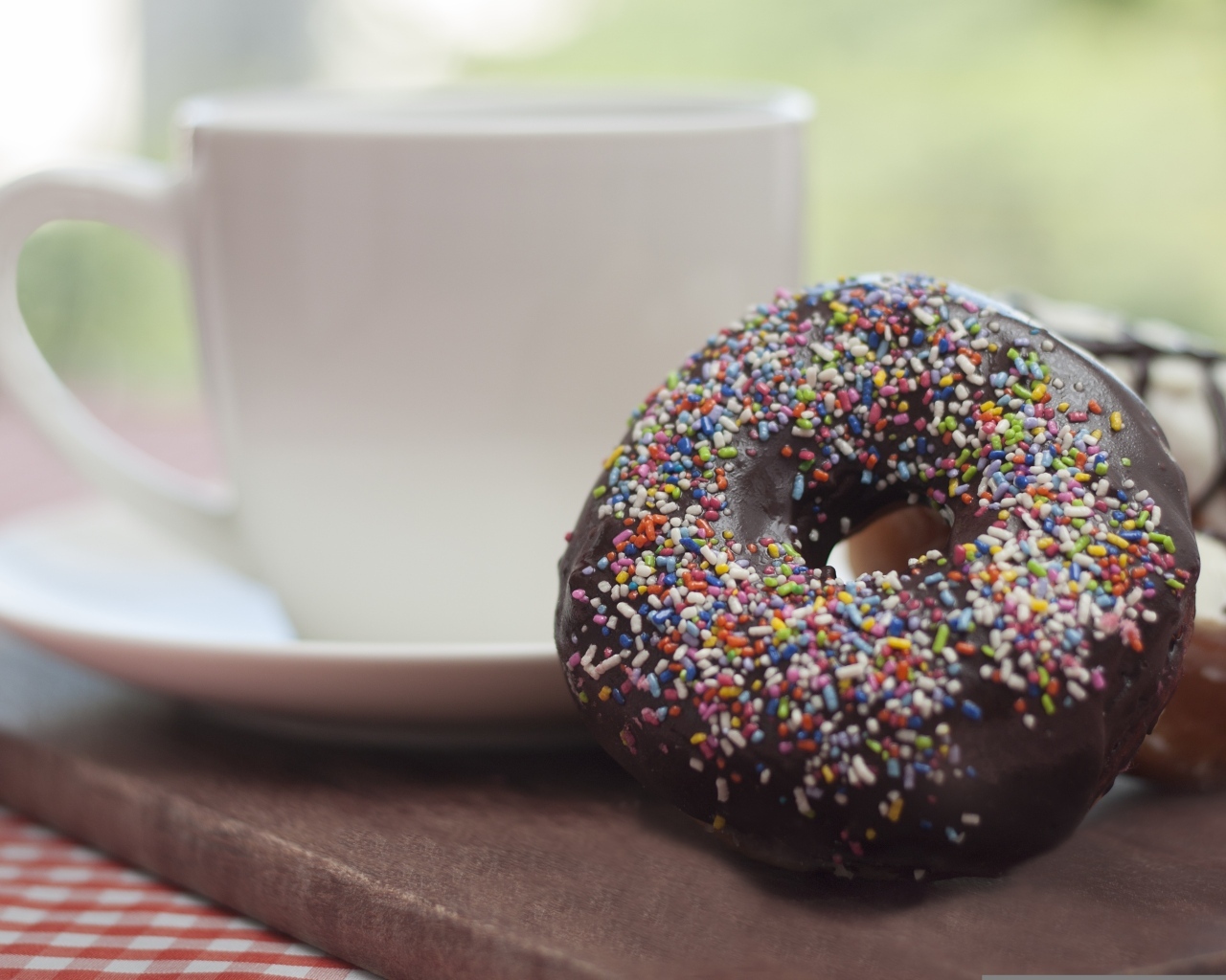 Донат с шоколадной глазурью и сладкой посыпкой на столе с чашкой чая