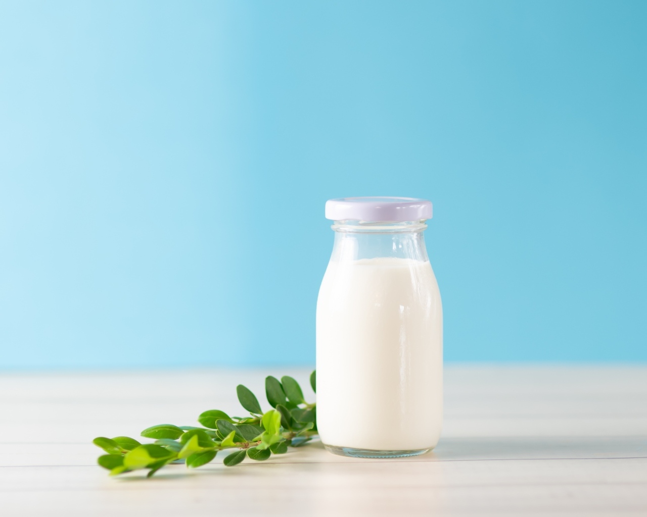 Бутылка молока с листьями на голубом фоне