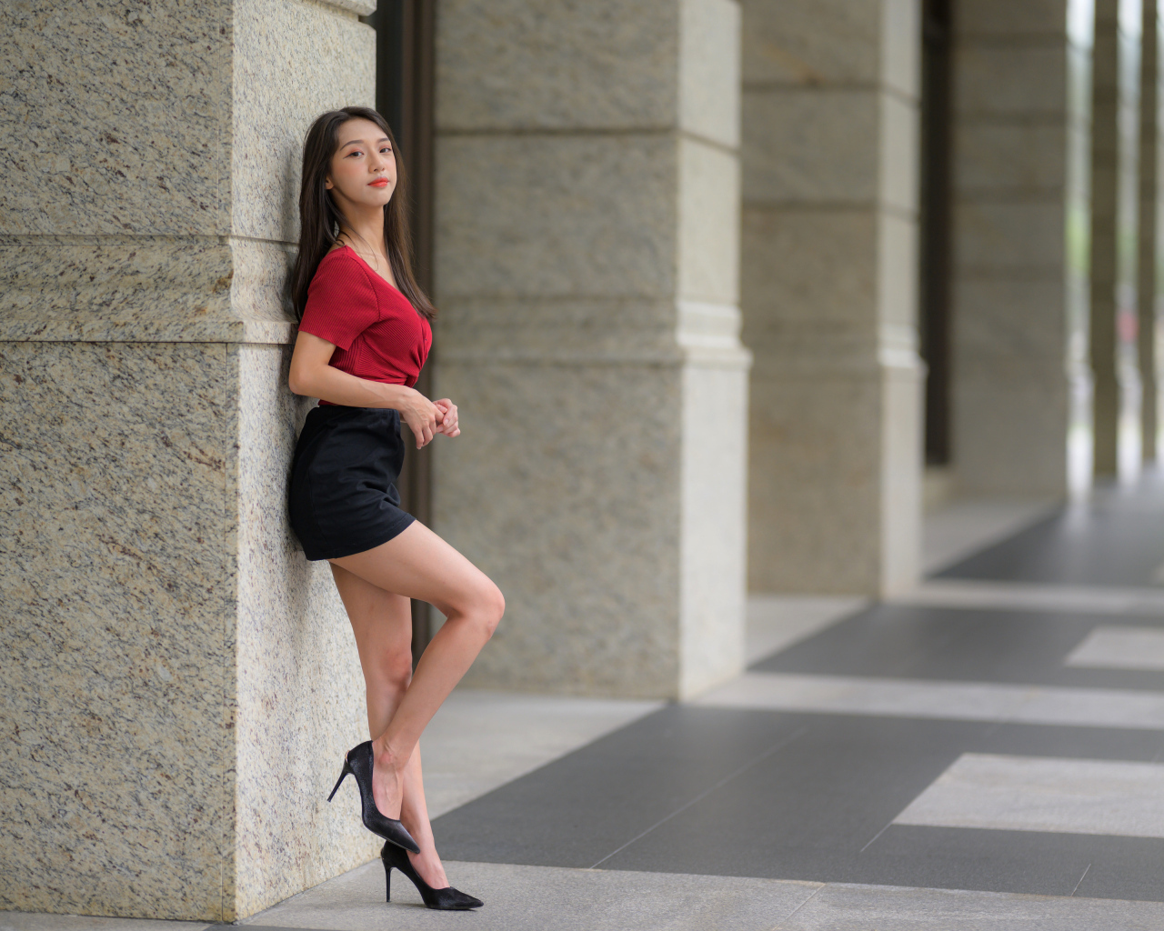 Азиатка в короткой черной юбке стоит у стены