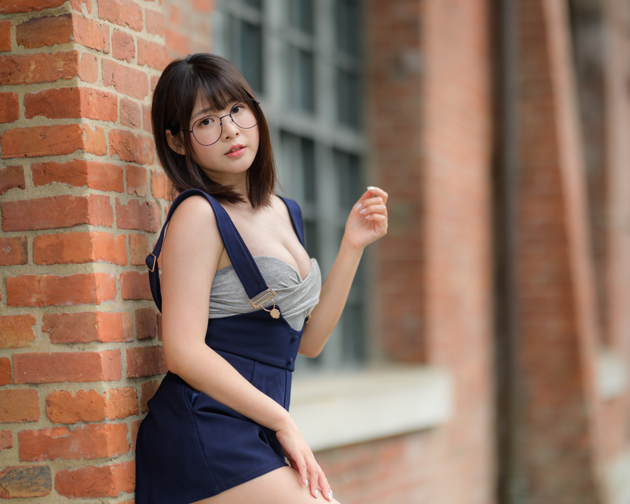 Азиатка в очках стоит у кирпичной стены